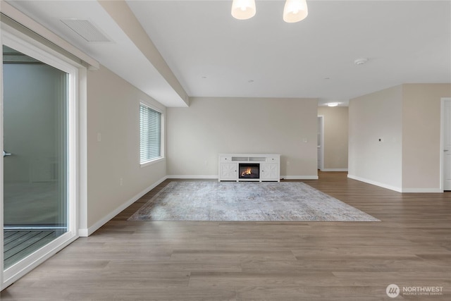 unfurnished living room featuring a glass covered fireplace, visible vents, baseboards, and wood finished floors