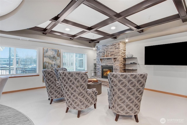 living room featuring a stone fireplace, plenty of natural light, and coffered ceiling