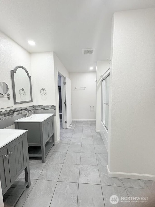 bathroom featuring visible vents, baseboards, two vanities, decorative backsplash, and a sink