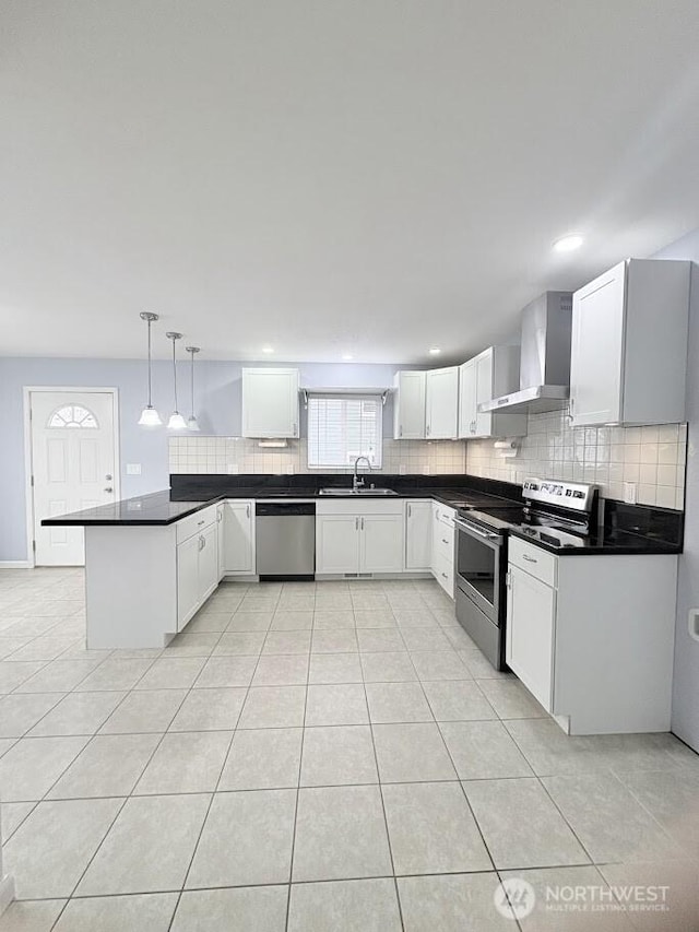 kitchen with a sink, backsplash, a peninsula, appliances with stainless steel finishes, and wall chimney exhaust hood