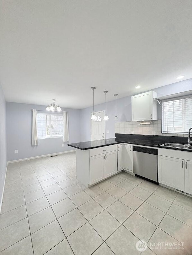 kitchen featuring dark countertops, a peninsula, stainless steel dishwasher, white cabinets, and a sink