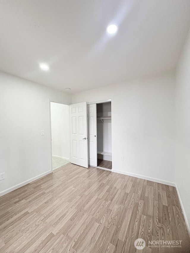 unfurnished bedroom with recessed lighting, light wood-type flooring, baseboards, and a closet