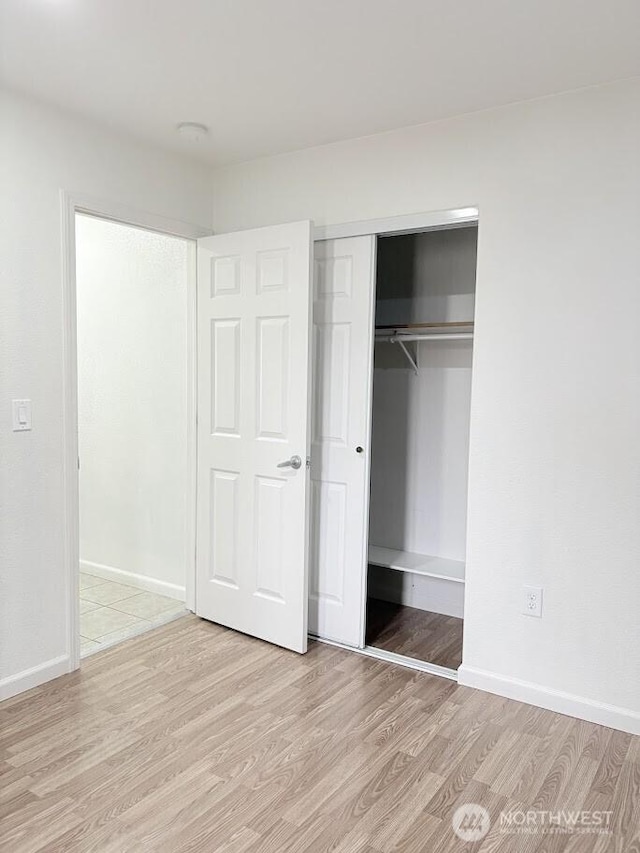 unfurnished bedroom featuring a closet, baseboards, and light wood-style floors