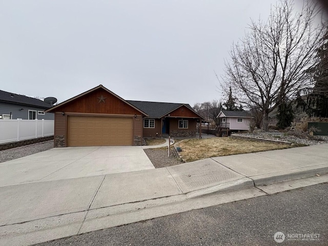 ranch-style home featuring concrete driveway, an attached garage, fence, and stone siding