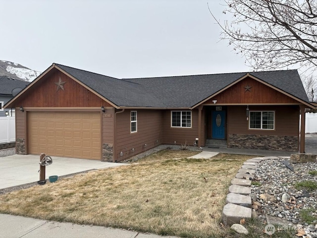 single story home with a front yard, roof with shingles, an attached garage, concrete driveway, and stone siding