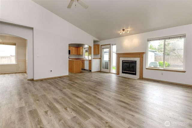 unfurnished living room featuring ceiling fan, baseboards, a fireplace, light wood-style floors, and arched walkways