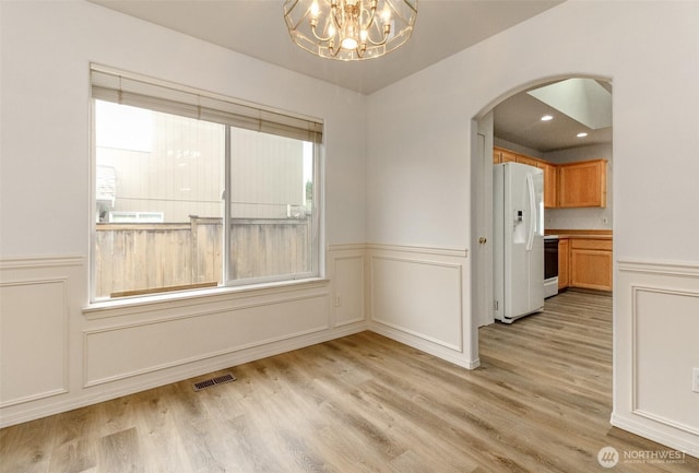 spare room with visible vents, light wood-style flooring, arched walkways, a decorative wall, and a chandelier