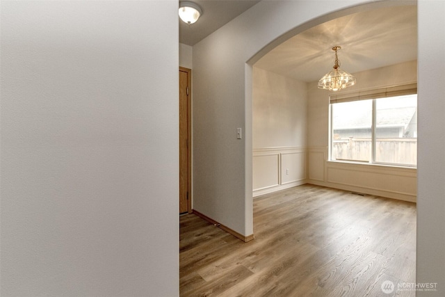 spare room with light wood-type flooring, a wainscoted wall, arched walkways, an inviting chandelier, and a decorative wall