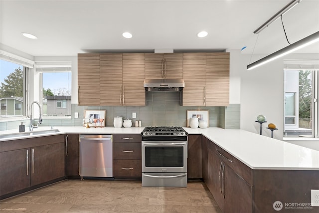 kitchen featuring a peninsula, a sink, stainless steel appliances, light countertops, and under cabinet range hood