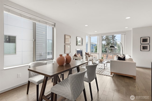 dining room featuring a glass covered fireplace, recessed lighting, light wood-style floors, and baseboards