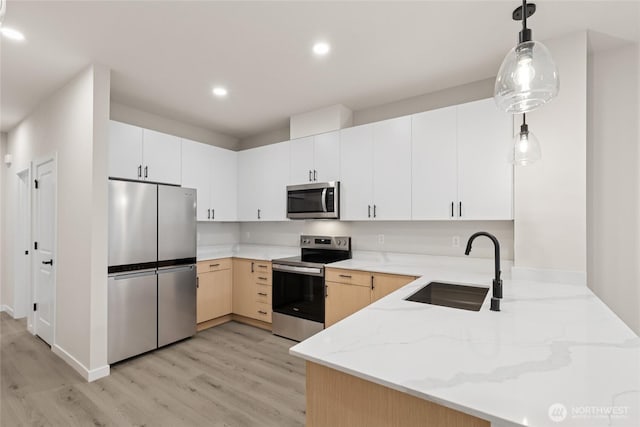 kitchen featuring light stone counters, light wood-style flooring, appliances with stainless steel finishes, a peninsula, and a sink