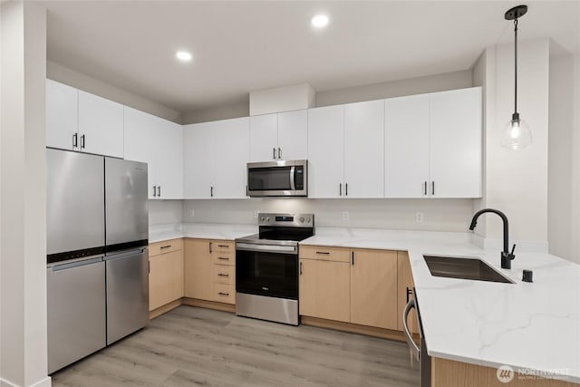 kitchen with light wood-type flooring, a sink, light stone counters, appliances with stainless steel finishes, and a peninsula