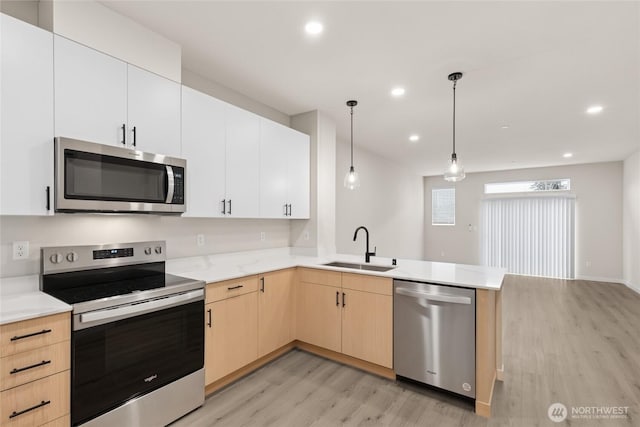 kitchen featuring a peninsula, a sink, light countertops, light wood-style floors, and appliances with stainless steel finishes