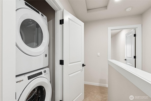 clothes washing area featuring laundry area, light colored carpet, stacked washer and clothes dryer, and baseboards