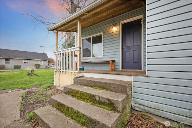 view of exterior entry with a porch and a lawn