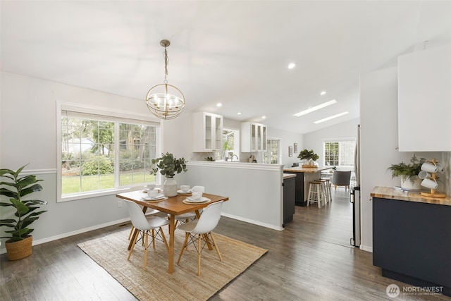 dining area with baseboards, dark wood finished floors, vaulted ceiling with skylight, recessed lighting, and a notable chandelier