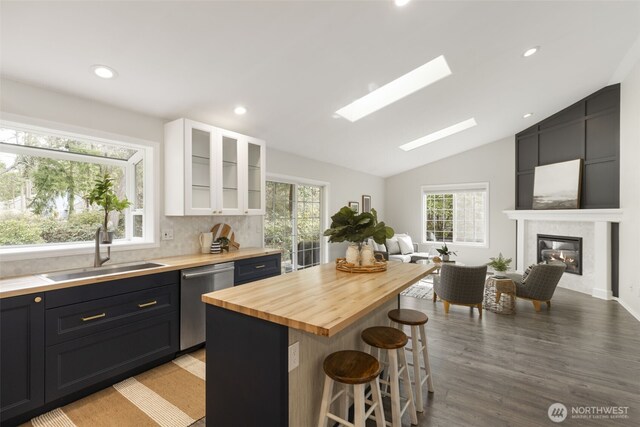 kitchen featuring a fireplace, a sink, butcher block countertops, stainless steel dishwasher, and a kitchen bar