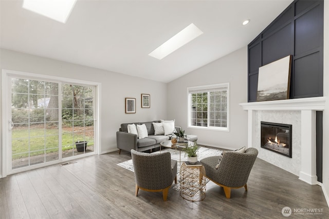 living area with vaulted ceiling with skylight, wood finished floors, baseboards, and a high end fireplace