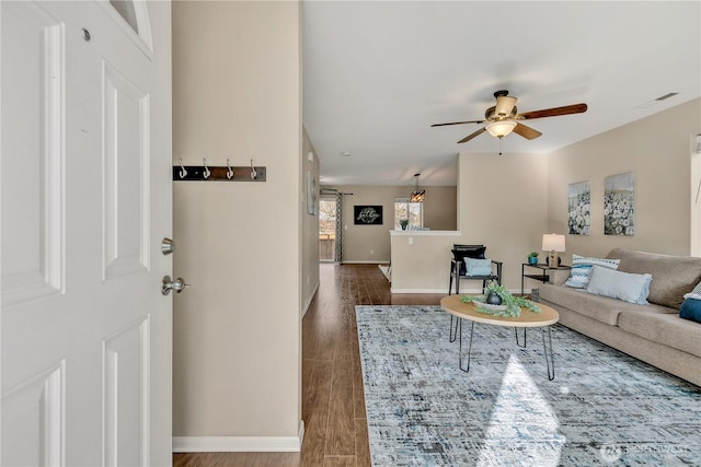 living area with baseboards, ceiling fan, and dark wood-style flooring