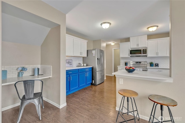 kitchen with blue cabinetry, a kitchen breakfast bar, wood finished floors, stainless steel appliances, and white cabinets