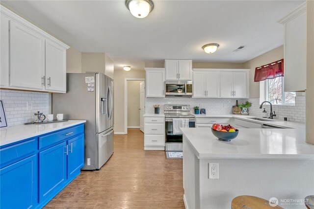 kitchen featuring blue cabinetry, light countertops, white cabinets, stainless steel appliances, and a sink