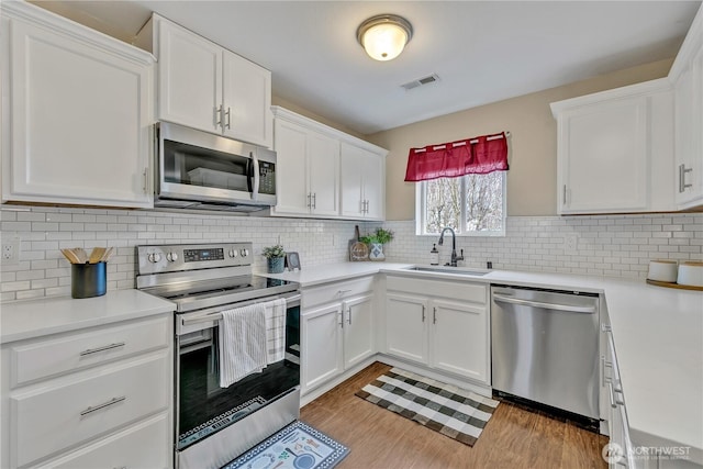 kitchen with visible vents, a sink, stainless steel appliances, light wood-style floors, and light countertops