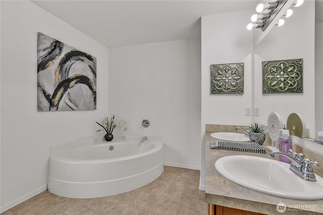 bathroom with a bath, double vanity, baseboards, and a sink