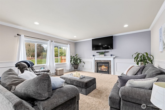 living area with a glass covered fireplace, wainscoting, carpet flooring, and crown molding