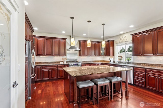 kitchen with dark wood-style flooring, stainless steel appliances, wall chimney exhaust hood, reddish brown cabinets, and a center island