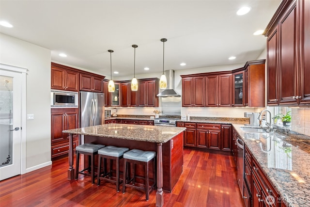 kitchen featuring dark wood-type flooring, a sink, appliances with stainless steel finishes, wall chimney exhaust hood, and glass insert cabinets