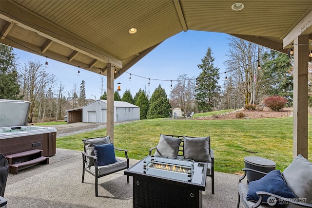 view of patio / terrace featuring a hot tub, a fire pit, a detached garage, and an outdoor structure