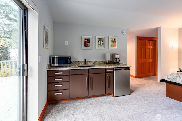 kitchen with light stone countertops, appliances with stainless steel finishes, light carpet, a sink, and baseboards
