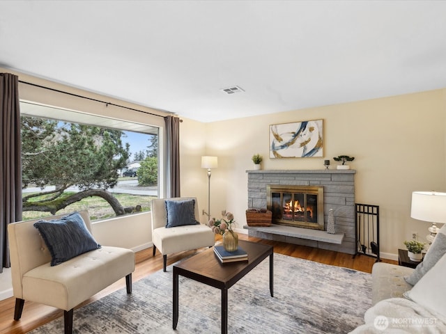 living area with a fireplace, wood finished floors, visible vents, and baseboards