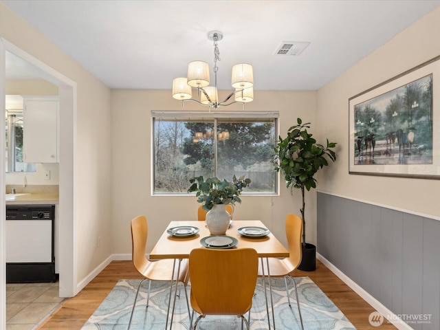 dining room featuring light wood-type flooring, visible vents, a notable chandelier, wainscoting, and baseboards