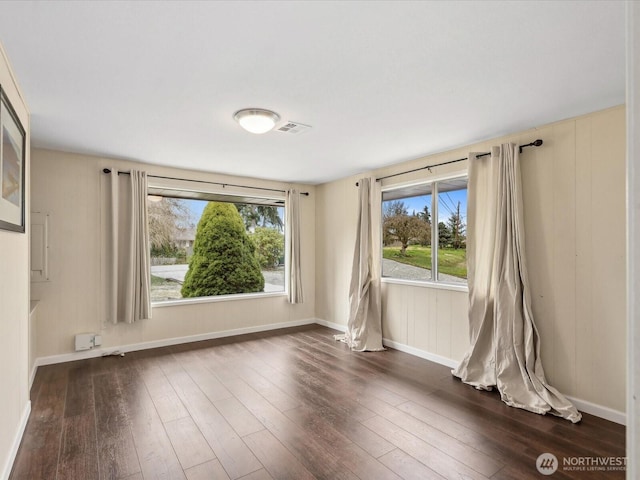 empty room with dark wood-style floors, visible vents, and baseboards