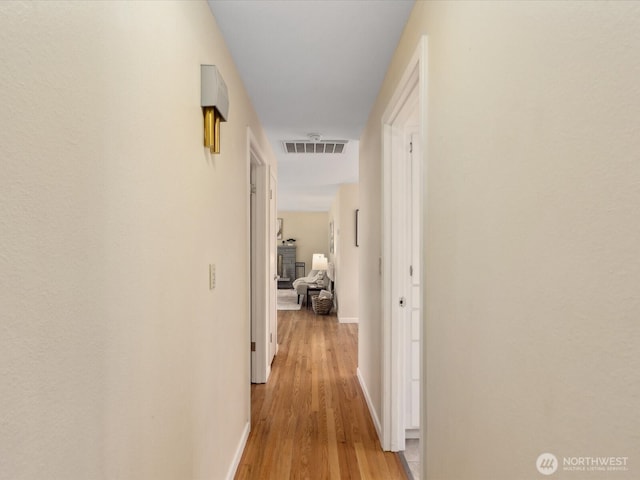 hall with light wood-style floors, visible vents, and baseboards