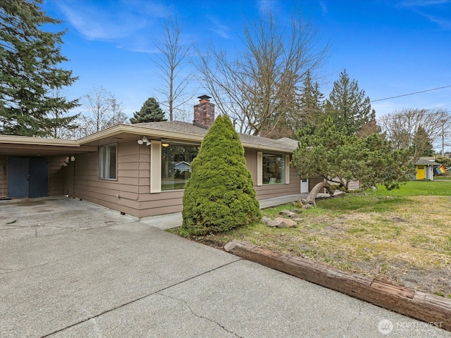 view of side of home with a yard, a carport, a chimney, and driveway