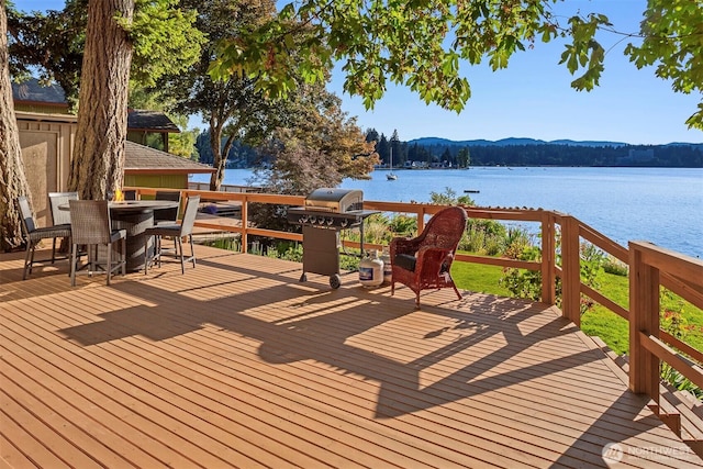 wooden deck with outdoor dining space, a water view, and a grill