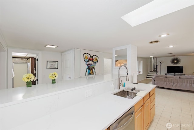 kitchen with a sink, light countertops, light tile patterned floors, a skylight, and stainless steel dishwasher