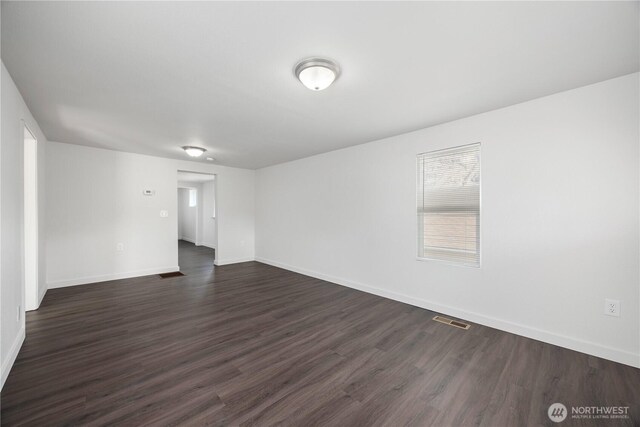 unfurnished room featuring visible vents, dark wood-type flooring, and baseboards