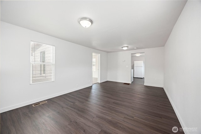 spare room with dark wood-style floors, visible vents, and baseboards