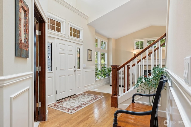 foyer entrance with wood finished floors, stairs, vaulted ceiling, wainscoting, and a decorative wall