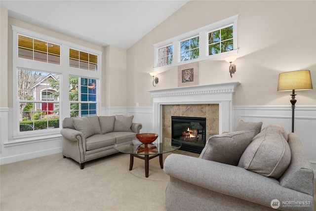 living area featuring a wainscoted wall, light colored carpet, high vaulted ceiling, and a premium fireplace