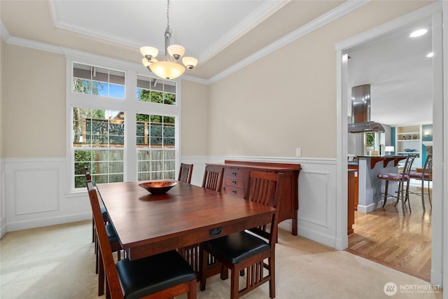 dining space with light carpet, a notable chandelier, a wealth of natural light, and a wainscoted wall