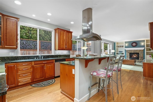 kitchen featuring light wood-type flooring, island exhaust hood, a sink, a kitchen breakfast bar, and dishwasher