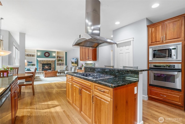 kitchen featuring dark stone counters, light wood-style flooring, brown cabinets, island exhaust hood, and stainless steel appliances