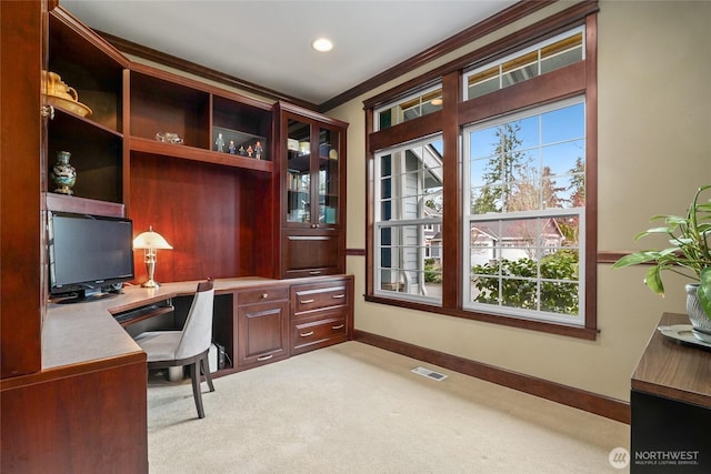 carpeted office space with crown molding, visible vents, built in desk, and baseboards