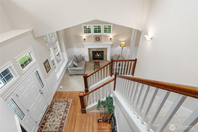 staircase featuring wainscoting, a healthy amount of sunlight, a tile fireplace, and wood finished floors