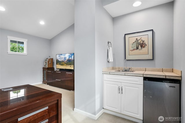 bar featuring baseboards, wet bar, freestanding refrigerator, a sink, and light carpet