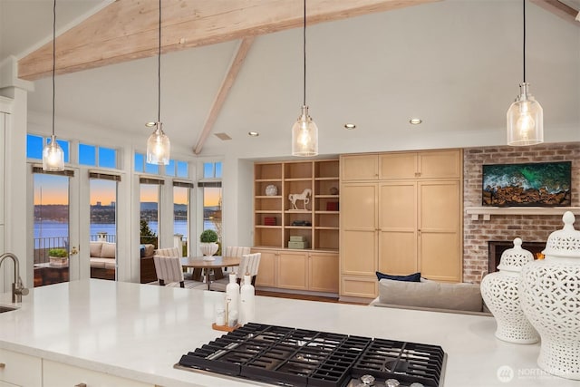 kitchen featuring pendant lighting, lofted ceiling with beams, open floor plan, light countertops, and stainless steel gas cooktop